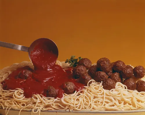 Freshly cooked spaghetti and meatballs with
        marinara being poured on with a ladel